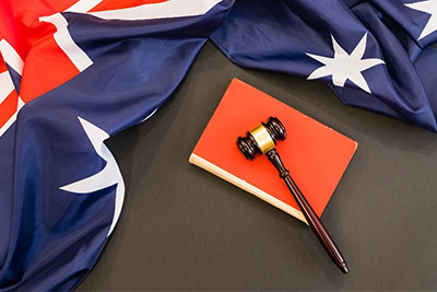 An Australian flag is draped on a black table next to a red book with a  judges gavel on top of it.