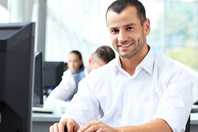 Man typing on a computer, looking into the camera and smiling.
