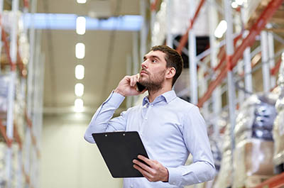 Man with clipboard and smartphone at a warehouse.